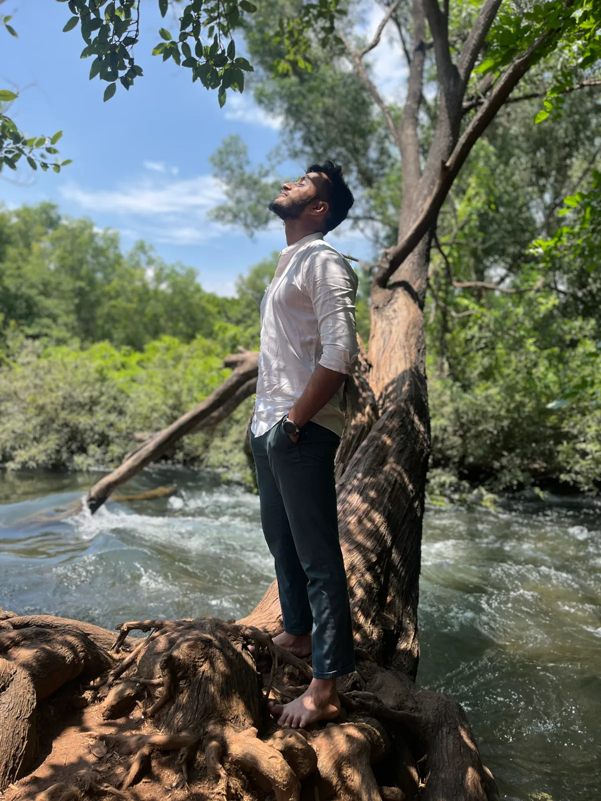 Rutvik standing on a tree root over a rushing river